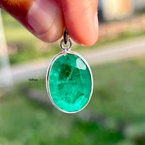 Può includere: Un ciondolo di smeraldo verde incastonato in una montatura ovale d'argento. Il ciondolo è appeso a una catena d'argento.