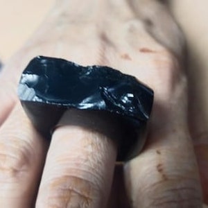 May include: A black obsidian ring with a rough, irregular shape. The ring is wide and flat, and it has a polished surface.