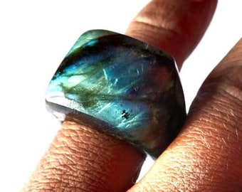 Puede incluir: Un anillo grande de forma cuadrada hecho de piedra de labradorita. El anillo tiene un color iridiscente azul, verde y negro.