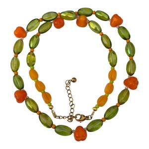 Könnte beinhalten: Eine Perlenkette mit abwechselnden ovalen, durchscheinenden olivgrünen Perlen und undurchsichtigen orangefarbenen fruchtförmigen Perlen. Die Kette enthält kleine runde orangefarbene und lindgrüne Zwischenperlen und einen goldfarbenen Karabinerverschluss.