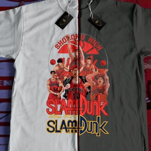 Può includere: Maglietta bianca e nera con una grafica di giocatori di basket dell'anime "Slam Dunk". La grafica include il testo "Shohoku High" e "Slam Dunk".