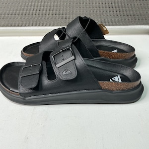 May include: Black leather sandals with adjustable buckles. The sandals have a cork footbed and a thick black sole. The sandals are designed for comfort and style, perfect for casual wear. The sandals are a size 9.