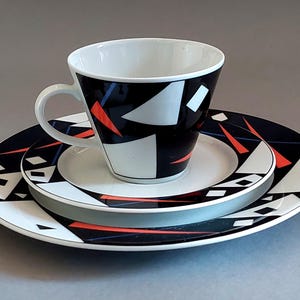 Peut inclure: Un ensemble tasse et soucoupe à thé avec un motif géométrique noir, blanc et rouge. La tasse et la soucoupe ont un design moderne avec des angles vifs et des couleurs vives.