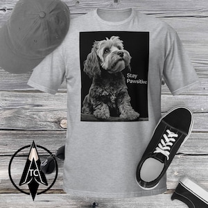 May include: A gray t-shirt with a black and white image of a small dog sitting on a branch. The text "Stay Pawsitive" is printed below the dog.