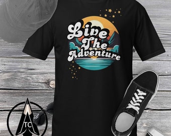 Op de afbeelding: Zwart T-shirt met een retro-grafische afbeelding van een berglandschap en de tekst "Live the Adventure".