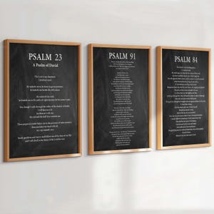 Op de afbeelding: Drie rechthoekige wandposters in lichte houten lijsten met zwarte schoolbord-stijl achtergronden en witte tekst. De prints tonen Psalm 23, Psalm 91 en Psalm 84, elk met de bijbehorende titel en de volledige bijbelse verzen in witte letters.