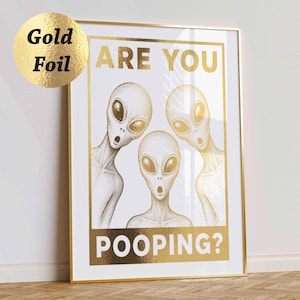 Könnte beinhalten: Gerahmter Kunstdruck mit drei Alien-Illustrationen aus Goldfolie auf weißem Hintergrund. Der Text "ARE YOU POOPING?" ist in Goldfolie gehalten. Das Kunstwerk ist in einem goldenen Metallrahmen gerahmt.