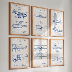 May include: Six framed vintage airplane patent prints. Each print features detailed blueprints in blue ink on a cream background. The frames are made of light brown wood, creating a classic aesthetic. The prints are arranged on a white wall.