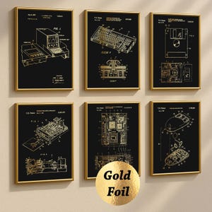 May include: Six framed gold foil prints on black backgrounds. The prints depict vintage computer components, including a keyboard, mouse, and circuit boards. Each print is in a gold frame, creating a cohesive set. The prints are arranged on a cream wall.
