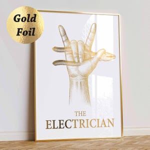 May include: Gold framed print with a hand gesture holding pliers, with the text "THE ELECTRICIAN" in gold. The artwork has a white background and a gold frame. A gold foil sticker is in the upper left corner.