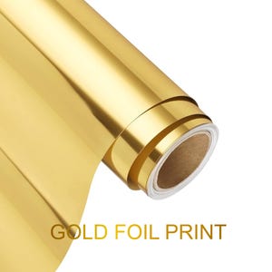 May include: A roll of metallic gold foil material with a smooth, reflective surface. The roll is partially unspooled, revealing a cardboard core. The text GOLD FOIL PRINT is displayed in gold capital letters below the roll of material.