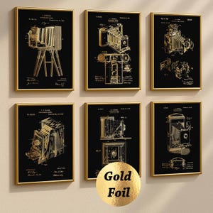 May include: Six framed art prints featuring gold-colored vintage camera patent illustrations on a black background. Each print is in a gold frame. The prints are arranged in two rows of three.