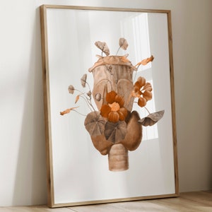 Può includere: Una stampa artistica incorniciata con un'illustrazione ad acquerello di una forma anatomica stilizzata adornata da fiori arancioni e fogliame marrone. L'opera d'arte ha una calda tavolozza di colori terrosi su sfondo bianco.