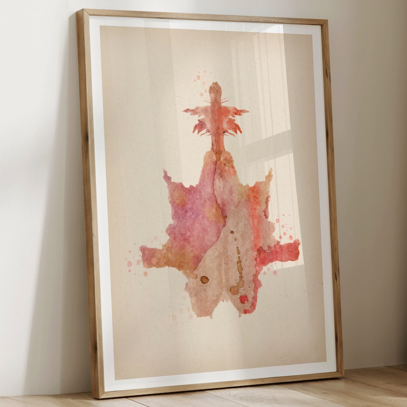 May include: A framed abstract watercolor painting in shades of pink, red, and brown. The painting features a symmetrical design with a central point and radiating lines.