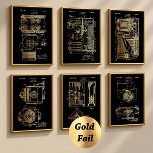 Può includere: Sei stampe brevettuali incorniciate con diagrammi tecnici color oro su sfondo nero. Le stampe sono in cornici dorate e sono disposte in due file da tre. Un adesivo dorato con le parole "Gold Foil" è in basso al centro.