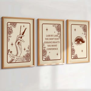 Op de afbeelding: Drie ingelijste kunstdrukken met een lichtbruine achtergrond en houten frames. De prints bevatten illustraties en tekst met een wimperthema, waaronder een hand die gereedschap vasthoudt, een oog met lange wimpers en inspirerende citaten.