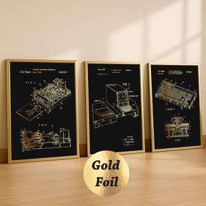 Puede incluir: Tres impresiones enmarcadas en papel de oro de diagramas de computadoras antiguas sobre un fondo negro. Las impresiones están en marcos dorados y presentan dibujos técnicos detallados de componentes de computadora. Las impresiones se exhiben sobre una superficie de madera clara.