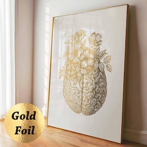 Puede incluir: Una impresión de arte mural rectangular vertical que presenta una ilustración en lámina de oro de un cerebro humano coronado por un grupo de flores en flor. La obra está enmarcada en un marco dorado fino sobre un fondo claro y liso.
