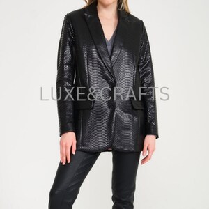 May include: A black snakeskin blazer with a single button closure. The blazer has a classic fit and a slightly longer length.