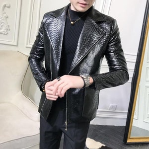 May include: A black, textured blazer with a reptile-skin pattern. The jacket has a notched lapel, a zip closure, and a tailored fit. The blazer is worn over a black turtleneck.