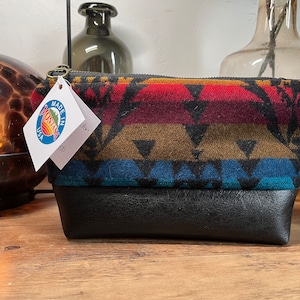 May include: A black and brown patterned zippered pouch with a black leather bottom. The pouch is made in Montana, USA.