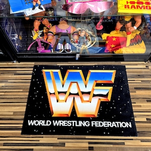 May include: Black rectangular mat featuring the World Wrestling Federation logo in blue, orange, and white. The words "WORLD WRESTLING FEDERATION" are printed in white below the logo. The mat has a starry background.