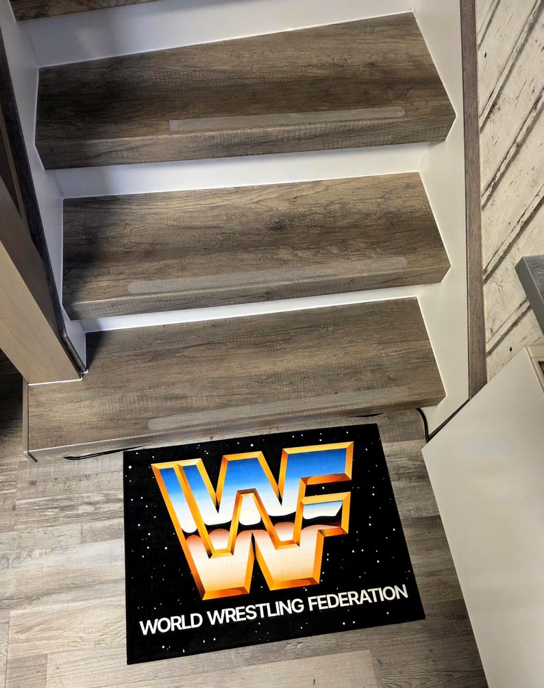 May include: Wooden staircase with three steps, featuring a gray-brown wood grain pattern. A black mat at the base displays the World Wrestling Federation logo in blue, orange, and white, with the text "WORLD WRESTLING FEDERATION".
