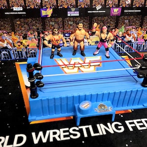 May include: A vintage World Wrestling Federation (WWF) wrestling ring playset with three action figures. The blue ring features red and white ropes, with a crowd backdrop. The WWF logo is visible on the ring.