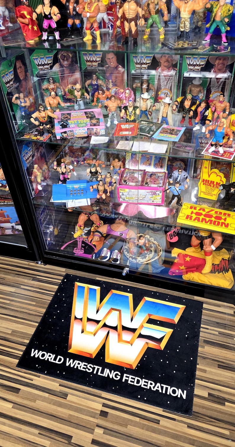 May include: A display case filled with vintage WWF (World Wrestling Federation) action figures and memorabilia. The case features various wrestlers, action figure packaging, and a black mat with the WWF logo and text.