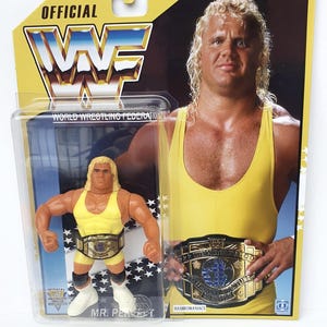 Pode incluir: Uma figura de ação do Mr. Perfect na embalagem original, apresentando o lutador com um collant amarelo e botas brancas com um cinturão de campeão. O cartão exibe o logotipo oficial da WWF, o texto "Ages 4 & Up" e uma foto.