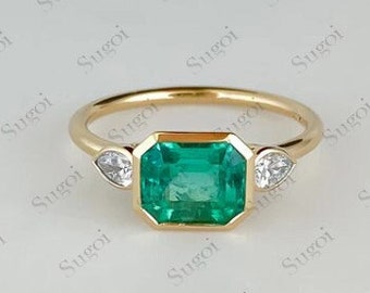 May include: A gold ring with a large emerald green gemstone surrounded by two smaller diamond-shaped gemstones.