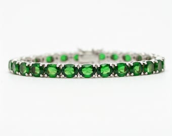 Puede incluir: Un brazalete de tenis de plata con una fila de piedras preciosas verdes ovaladas.