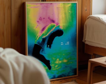 Pode incluir: Uma impressão de arte emoldurada com uma silhueta de uma pessoa em um design abstrato e colorido. A obra de arte apresenta uma paleta vibrante de azuis, verdes, rosas e amarelos. O texto "WE ARE NOT ALONE" é visível no canto inferior direito.