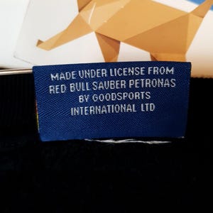 Puede incluir: Una etiqueta azul con texto blanco que dice "Made under license from Red Bull Sauber Petronas by Goodsports International Ltd."