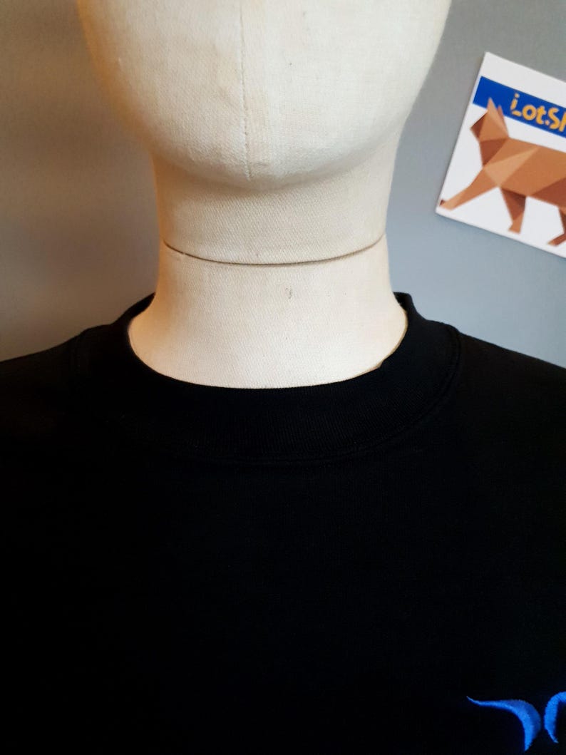 Puede incluir: Sudadera negra con un dise&ntilde;o bordado en azul en la esquina inferior derecha.