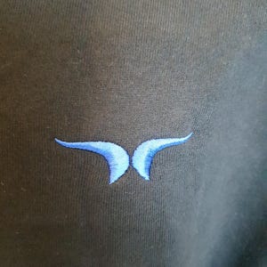 Puede incluir: Una sudadera negra con un dise&ntilde;o de mariposa bordada en azul.