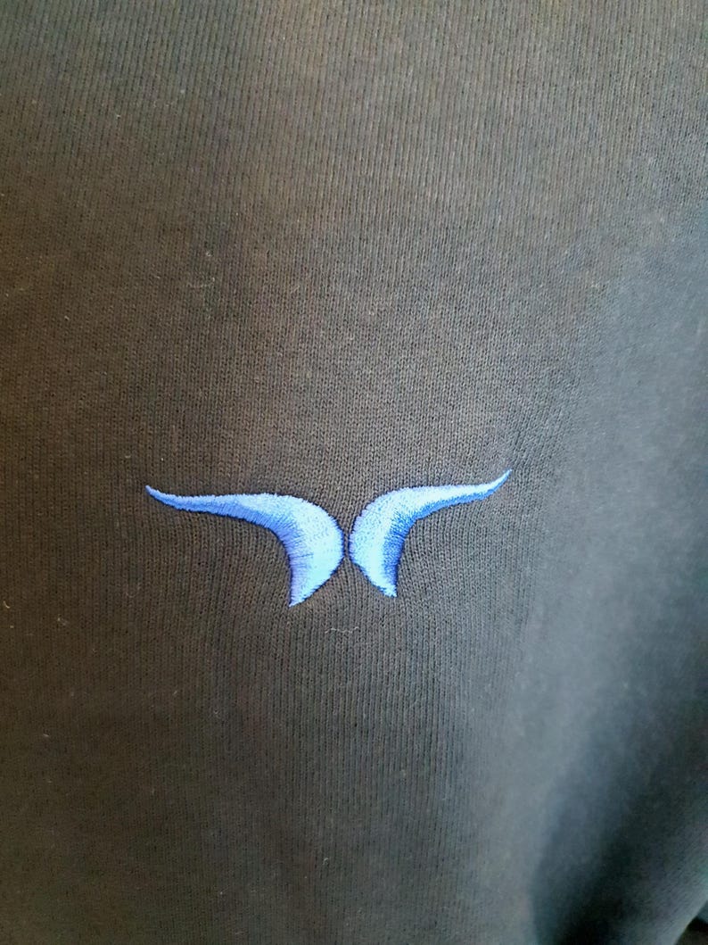 Puede incluir: Una sudadera negra con un dise&ntilde;o de mariposa bordada en azul.