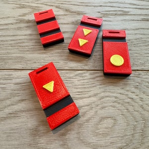 May include: Four red and black rectangular objects with yellow triangle and circle accents. The objects are arranged on a light wood-grain surface. Each object has a slot at the top.