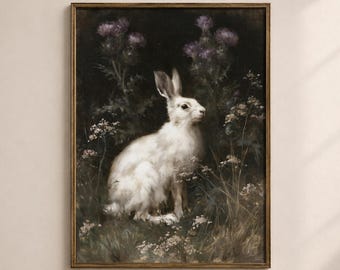 May include: A framed wall art print featuring a white rabbit sitting in a dark, moody field of purple thistle flowers and wild grasses. The painting uses a muted color palette with deep shadows and soft highlights on the rabbit's fur.