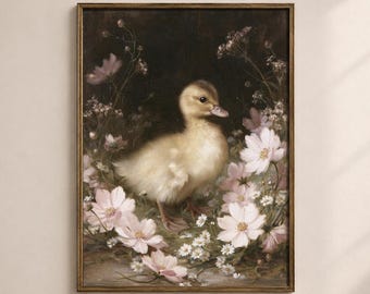 May include: A framed wall art print featuring a fluffy yellow duckling standing amidst a cluster of soft pink cosmos flowers and small white blossoms against a dark, moody background. The artwork is enclosed in a thin, dark-toned frame.