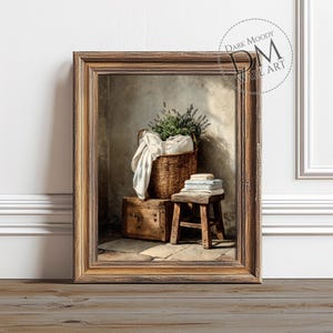 Peut inclure: Une impression encadrée représente une scène rustique avec un panier en osier rempli de verdure et de linge blanc. Un petit tabouret en bois contient une pile de serviettes pliées. Une boîte en bois est située sous le panier. L'œuvre est étiquetée "DARK MOODY WALL ART".