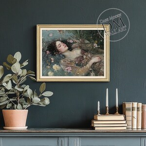 May include: A framed wall art print featuring a woman floating in water surrounded by flowers. The artwork has a gold frame and is set against a dark teal wall. The text "Dark Moody Wall Art" is in the upper right corner.