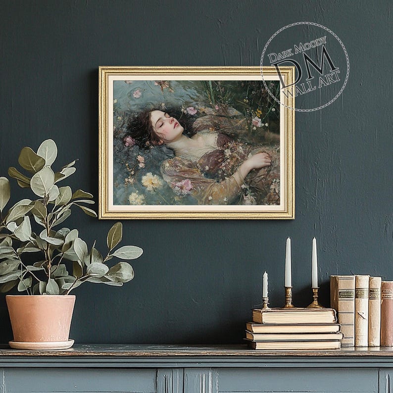 May include: A framed wall art print featuring a woman floating in water surrounded by flowers. The artwork has a gold frame and is set against a dark teal wall. The text "Dark Moody Wall Art" is in the upper right corner.