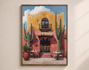 May include: A framed print of a Southwestern-style building with a yellow facade and a red exterior. Tall cacti flank the building, and small tables and chairs are set up outside. The sky is blue with fluffy white clouds.
