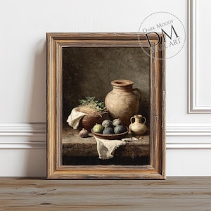 May include: A framed still life painting depicting a rustic wooden table with a large earthenware jug, a small vase, and a bowl of figs. A basket of greenery and a white cloth complete the composition. The frame is a warm brown colour.