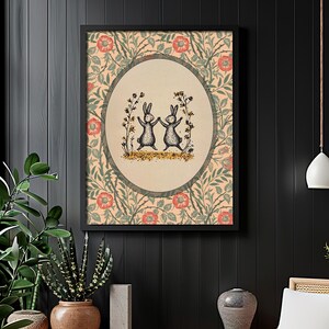 Pode incluir: Uma impress&atilde;o emoldurada com um padr&atilde;o floral vintage em tons de verde, vermelho e creme. O centro da impress&atilde;o apresenta um design circular com dois coelhos pretos e brancos dan&ccedil;ando em um campo de flores.