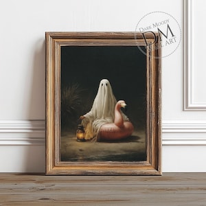 May include: Framed artwork depicting a ghost in a white sheet beside a pink flamingo inflatable ring. The ghost holds a lantern. The artwork is in a gold-toned wooden frame. The text "DARK MOODY WALL ART" is in the upper right corner.