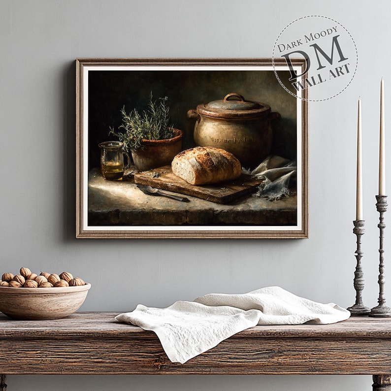 Op de afbeelding: Een ingelijste print van een stilleven met een rustieke keukensc&egrave;ne. Het kunstwerk toont een brood op een houten snijplank, een keramische pot, een klein glas vloeistof en een kruidenplant in een pot. De print is getiteld "Dark Moody Wall Art."