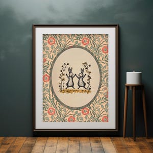 Pode incluir: Uma impress&atilde;o emoldurada com um padr&atilde;o floral vintage em tons de verde, rosa e creme. Dois coelhos pretos dan&ccedil;am em c&iacute;rculo dentro de um oval de cor creme. Os coelhos s&atilde;o cercados por pequenas flores amarelas.