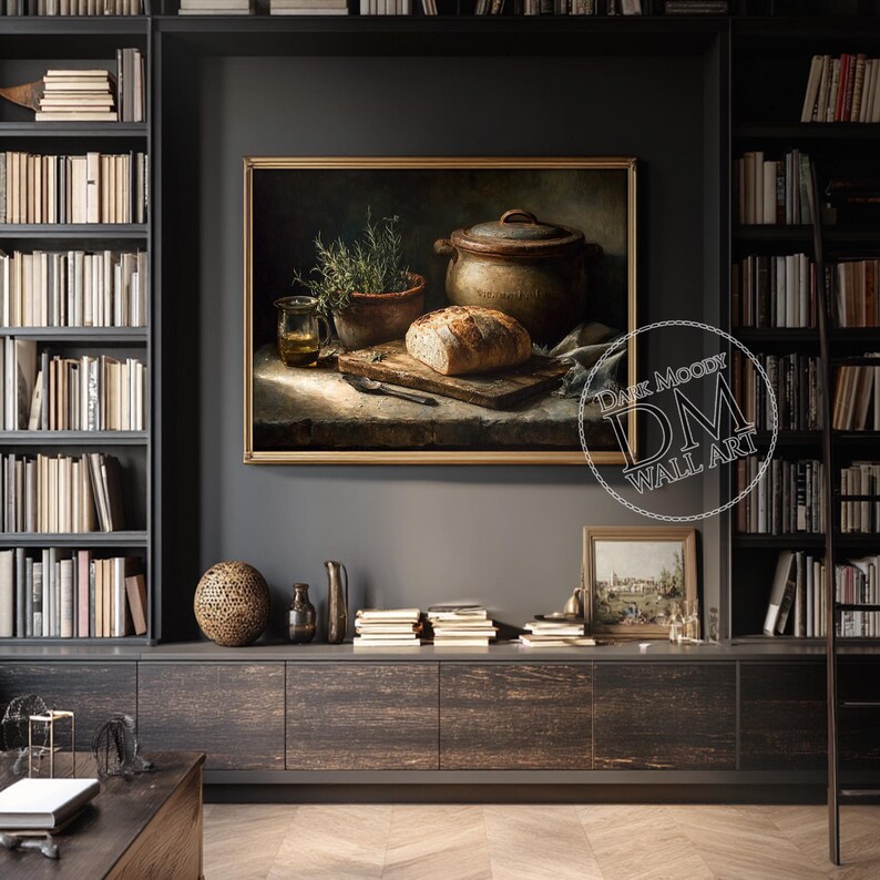 Op de afbeelding: Een ingelijst stilleven schilderij met een brood op een houten snijplank, een kleipot en een kruidenplant in een pot. Het schilderij heeft een warm kleurenpalet en wordt getoond op een donkergrijze muur. De tekst "Dark Moody Wall Art" is zichtbaar.